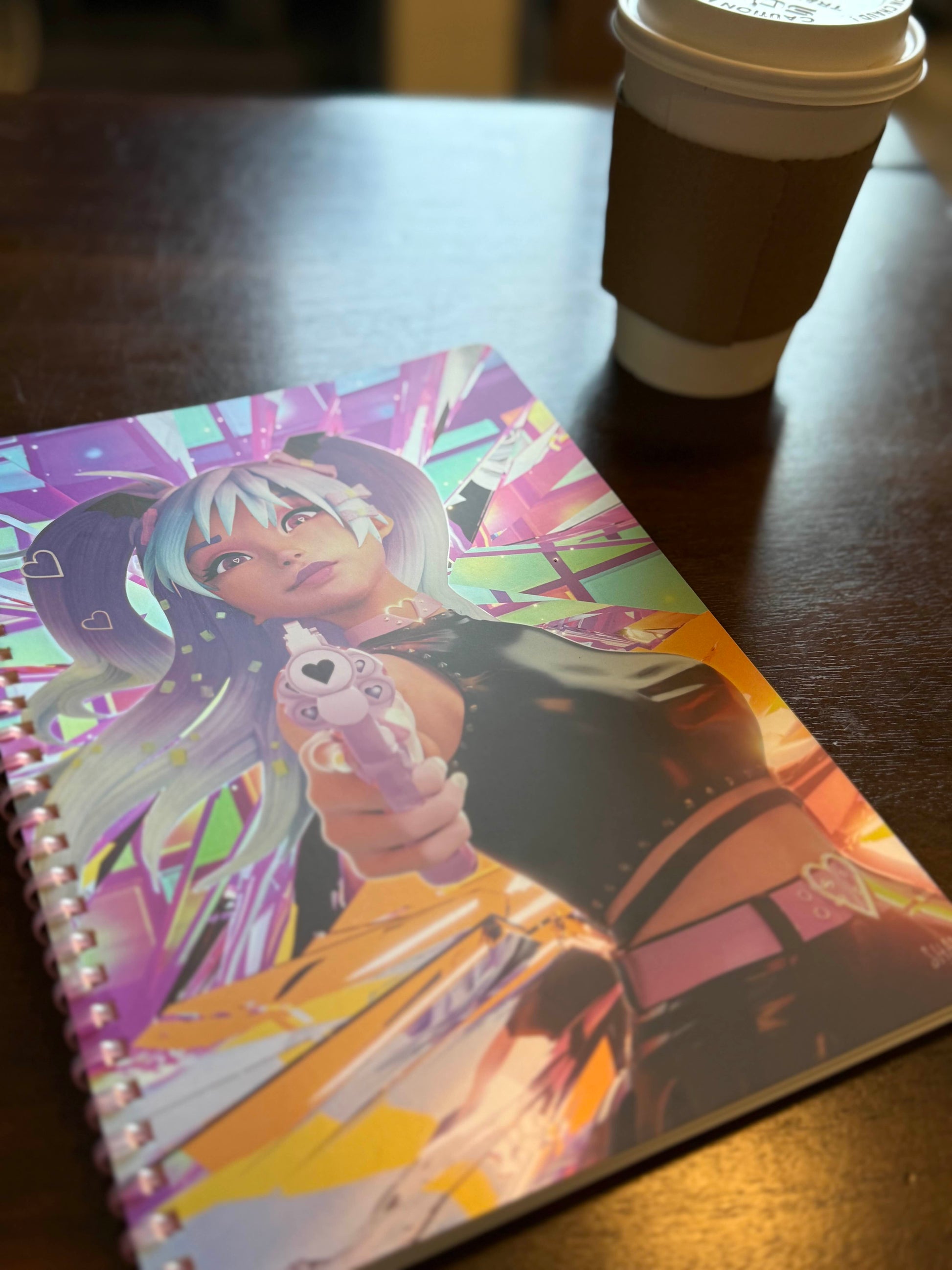 Bad Vibes holographic spiral notebook with glossy anime girl cover shown on wooden table next to coffee