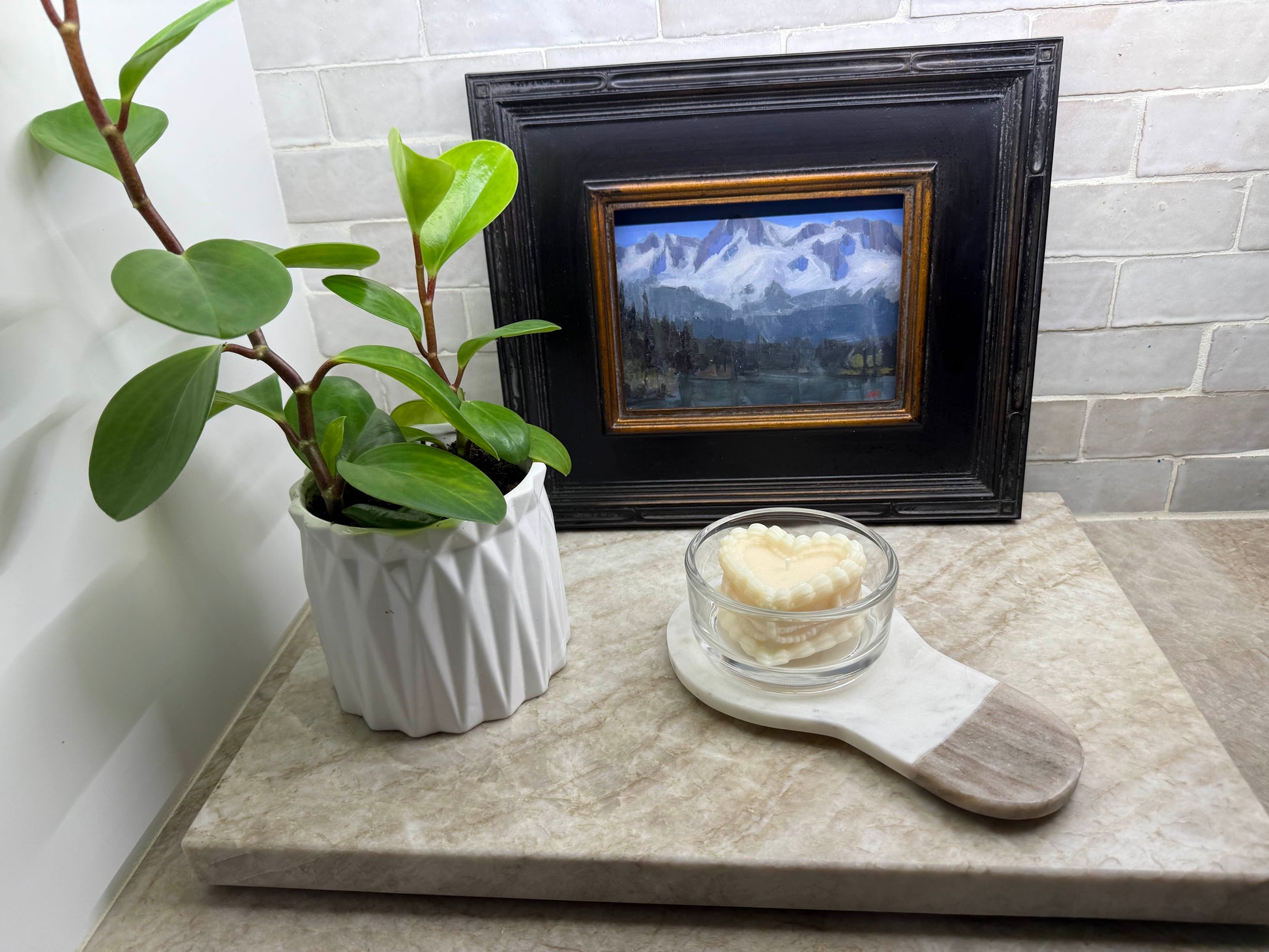 vintage coquette cake candle in glass dish on marble serving board styled with potted plant and framed landscape painting