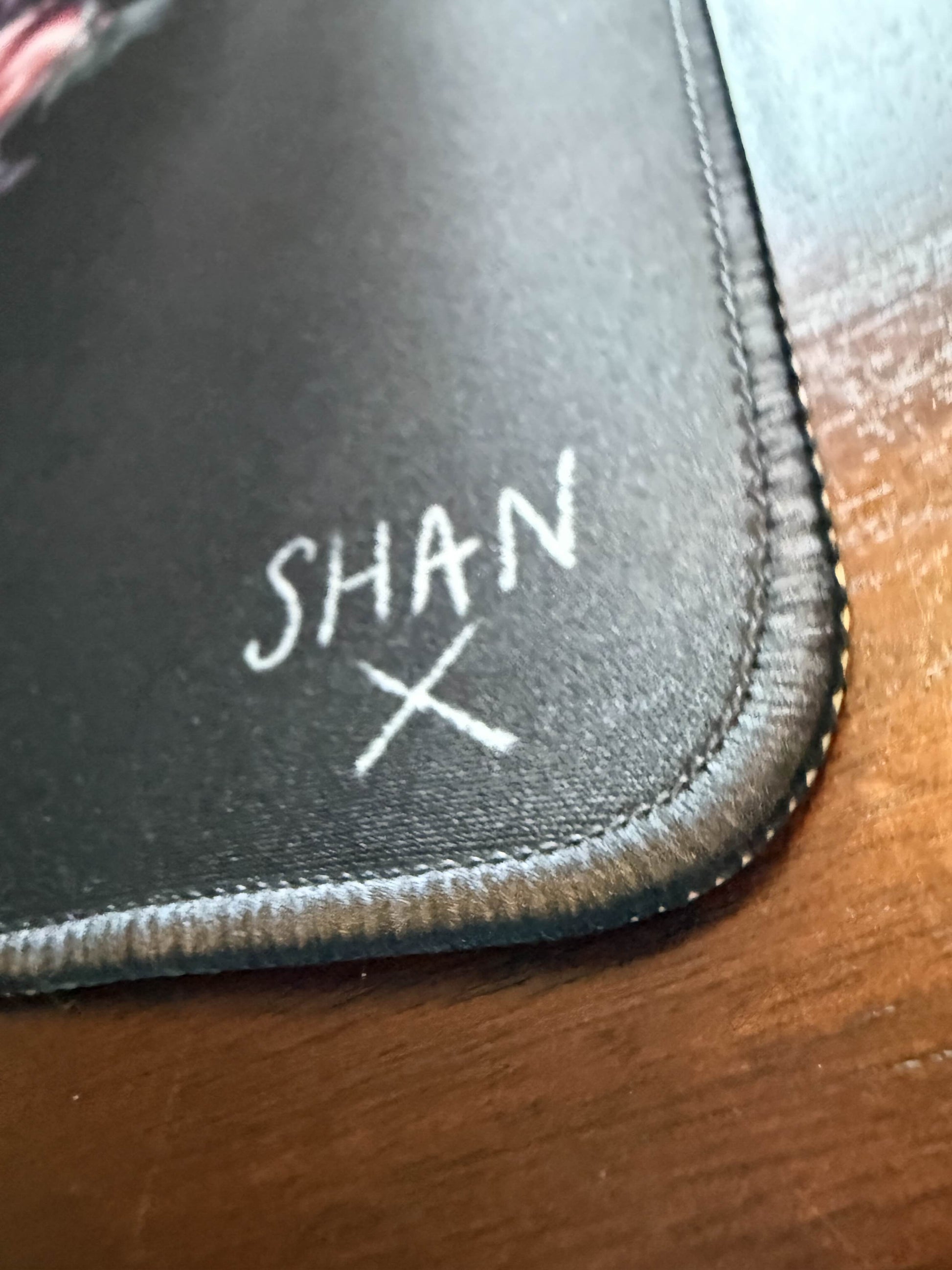 Black signed fabric desk mat with stitched edge reading SHAN X on wood surface home decor by Bad Vibes